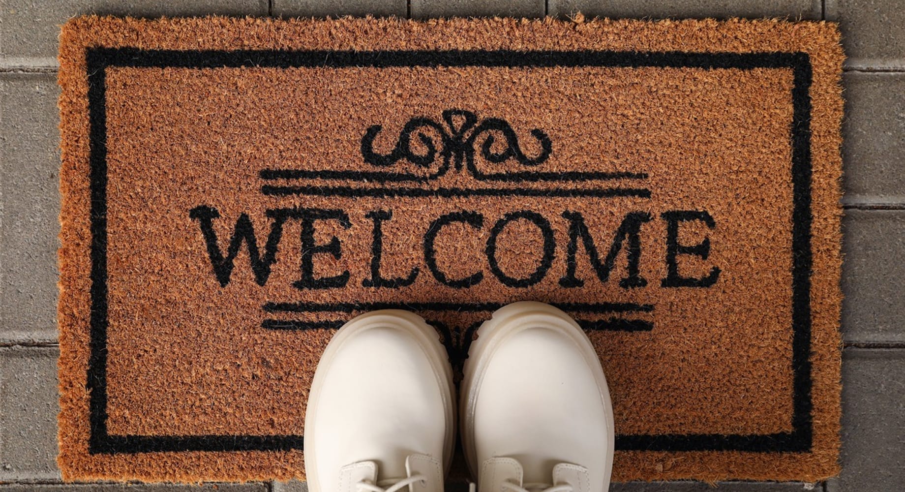 A pair of white lace-up boots standing on a natural coir doormat printed with the word WELCOME