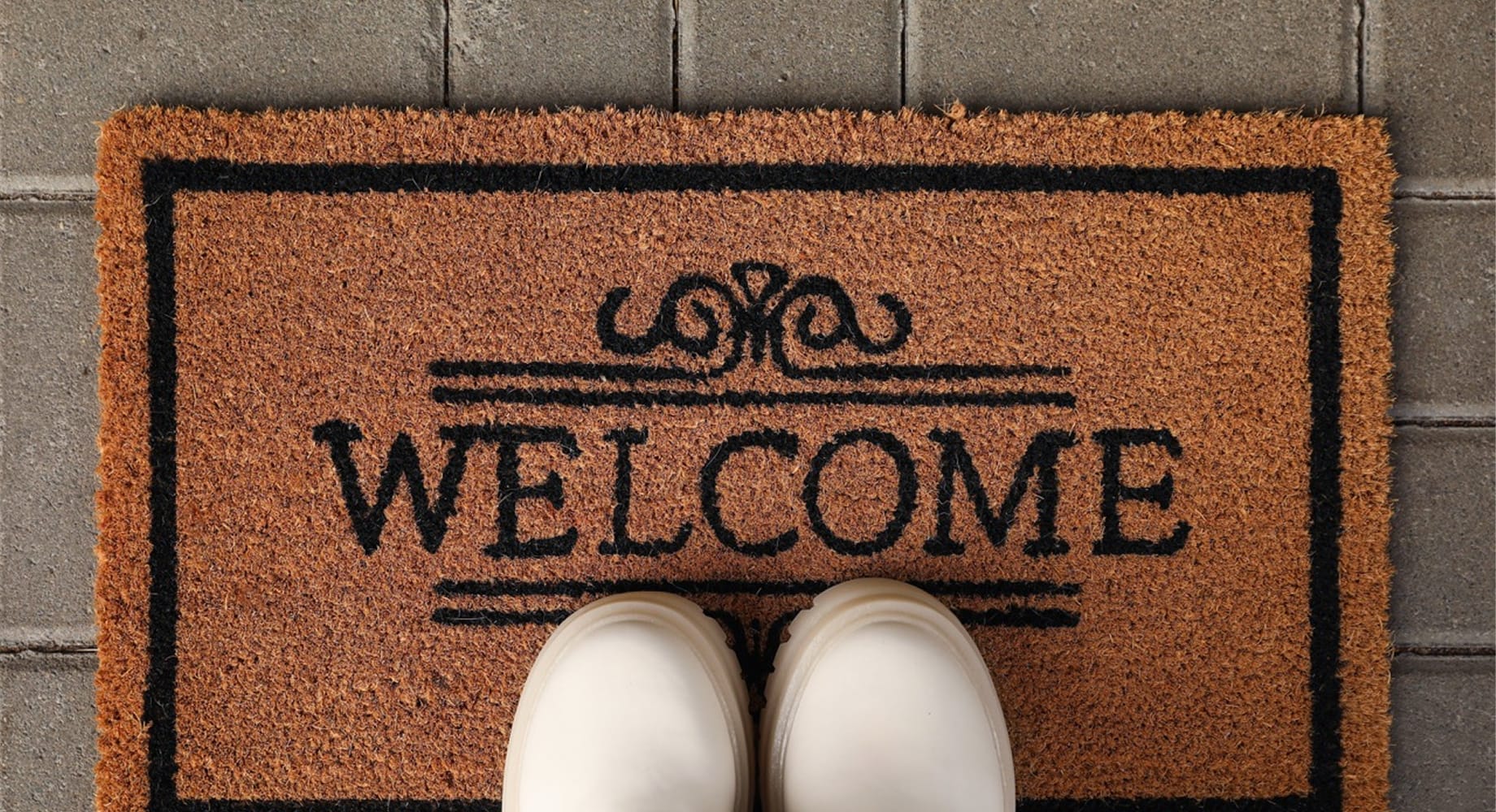 A pair of white lace-up boots standing on a natural coir doormat printed with the word WELCOME
